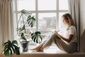 Vrouw zit ontspannen bij het raam met notitieboekje – moment van reflectie tijdens Ayurveda dosha test